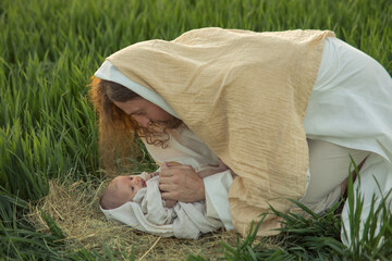 Saint Joseph bents over baby Jesus lying on grass.