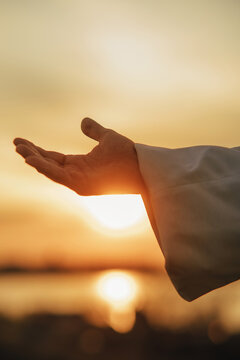 Jesus Christ reaching out his hand at sunset.