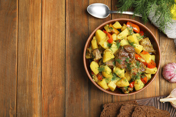 Tasty cooked dish with potatoes in earthenware served on wooden table, flat lay. Space for text