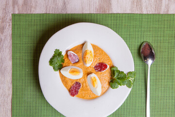 Vegetable cream soup with egg, salami slices, and cilantro on a white plate on a green napkin on the table.