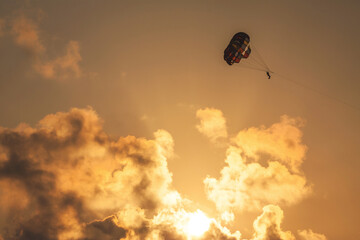 Parasailing at sunset. Silhouette of a person with parachute against evening orange sky with clouds.