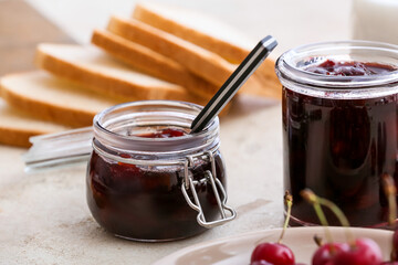 Jars with tasty cherry jam on table, closeup