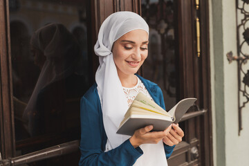 Portrait of young muslim woman wearing hijab reading book outdoors