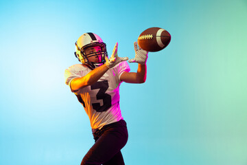 One male American football player training isolated on blue studio background in neon light....