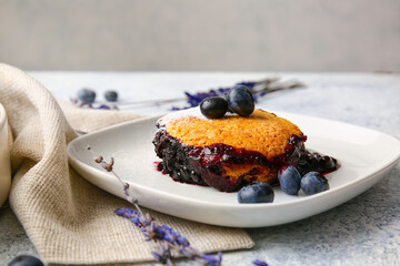 Plate with piece of blueberry cobbler and lavender on light background, closeup