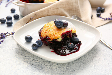 Plate with piece of blueberry cobbler and lavender on light background, closeup