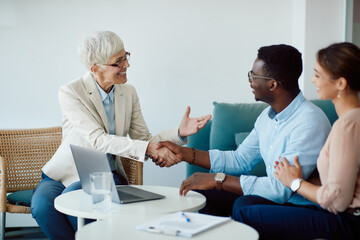 Happy mature financial advisor shaking hands with a couple after successful agreement.