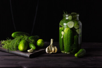 Pickles in a glass jar with garlic on a dark wooden table, copyspace.