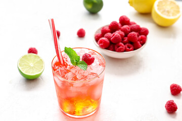 Glass of tasty lemonade and bowl with raspberry on light background