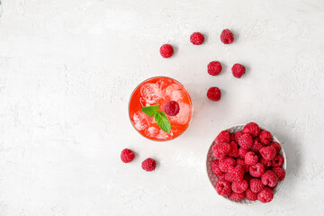 Glass of tasty lemonade and bowl with raspberry on light background