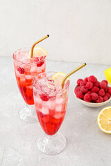 Glasses of tasty lemonade and bowl with raspberry on light background