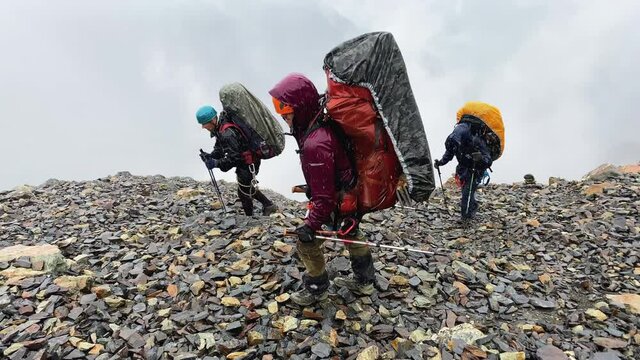 Drenched tourists with large backpacks walk on slippery stones in heavy rain. Climbing Kazbek from the north, from the side of Russia. Hike across the Caucasus.