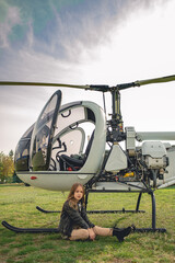 Tween girl sitting on green grass of flying field near helicopter