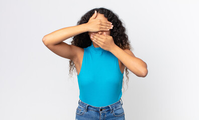 pretty hispanic woman covering face with both hands saying no to the camera! refusing pictures or...