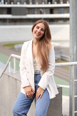 Young sensual fair-haired woman near metal railing at stadium