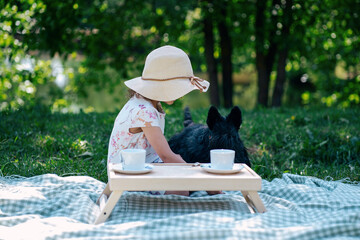 Little girl in straw hat with scotch terrier dog at picnic