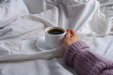 Girl holding a cup of coffee in bed. Breakfast in bed. Interior. Cosiness.