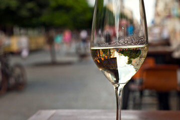 Glass of white wine close up. Alcoholic drink on a wooden table on a background of the city. Transparent wine on the summer terrace of the restaurant. Blurred people in the background.