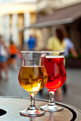 Glass of red and white wine close up. Alcoholic liqueur on a wooden barrel on a background of the city. Blurred people in the background.