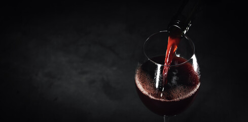 Naklejka na ściany i meble red wine pouring into a glass from bottle on a black background. banner copy space
