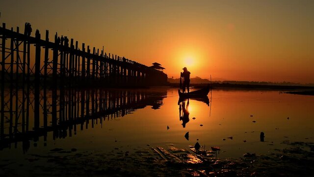 Silhouette fisherman throwing net casting fish in early morning with wooden boat with a flock of birds, Fisherman life style