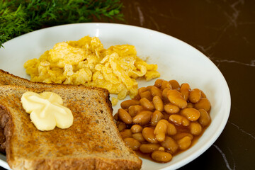 Close-up of a healthy breakfast with toasted bread, butter, baked beans and scramble eggs. Selective focus points