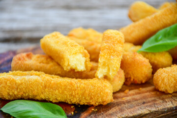 Vegetarian cheese breaded  oven baked  mozzarella sticks with  fresh basil on wooden background 