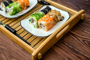 Several sushi on a white plate standing on a brown wooden background
