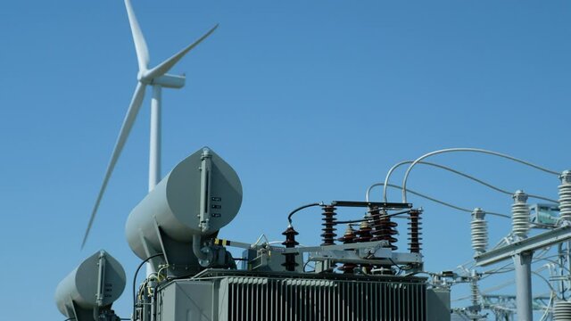 Wind generator stays idle in breathless weather and high potential power transformer at substation on foreground against blue sky