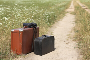 binoculars with large and small suitcases on a field road on a summer day. promising direction for...