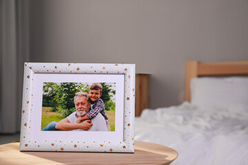 Framed family photo on wooden table in bedroom. Space for text