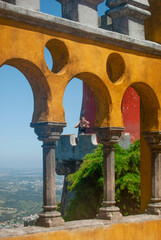 A woman posing at the balcony of Pena Palace seen through moorish styled arches - Sintra, Portugal...