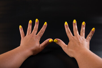 Girl's hands with manicure. Yellow nails on black background. Spa manicure service.