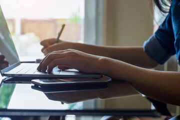 Young female student work on laptop computer and writing on notebook at workplace. Online learning, distance woring, telework or remote working concept.