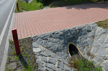 Sewer bridge through a ditch by the road. concrete hole with surroundings of stone paving. grassy...