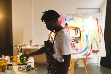 African american male painter at work holding paint in art studio