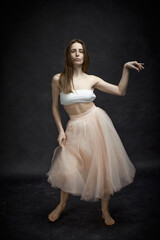 Young girl in white top and peach skirt dancing in black old textured studio