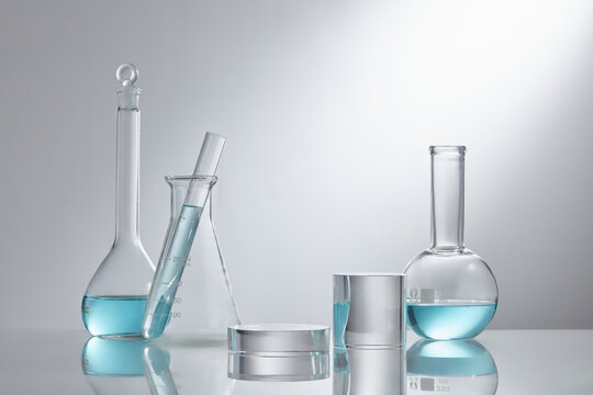 Stage showcase cosmetics on glass pedestal modern in laboratory equipment. Laboratory glass equipment with blue water ingredients on white background. Research and development cosmetics concept

