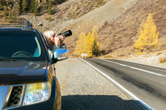 Mature woman taking photo from her car. Woman travel autumn.