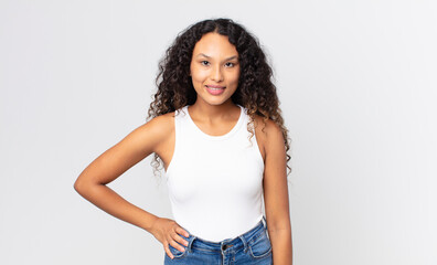 pretty hispanic woman smiling happily with a hand on hip and confident, positive, proud and...