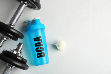 Shaker with abbreviation BCAA (Branched-chain amino acid), dumbbells and powder on white table,...