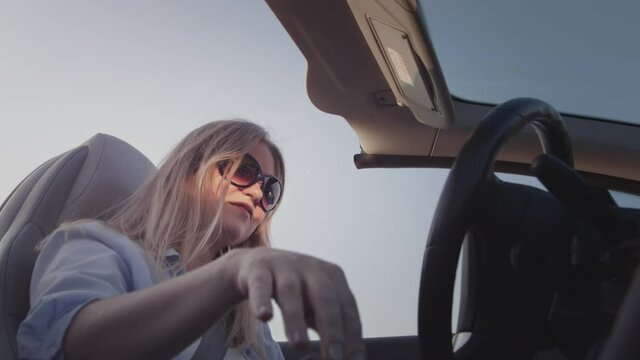 A young girl driving a convertible switches the automatic transmission. Begins to move. The beginning of a journey, a road trip. Grabs the selector joystick with his hand. Woman driving a car.