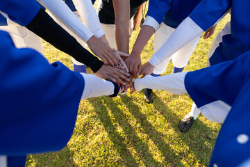 Diverse group of female baseball players making hand stack on sunny baseball field