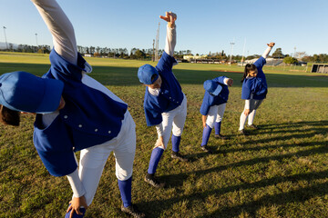 Diverse group of female baseball players warming up on field, stretching from the waist