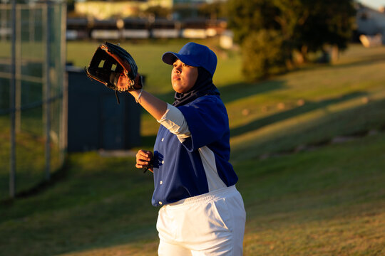 Mixed race female baseball player on sunny baseball field reaching to catch ball during game