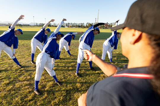 Diverse group of female baseball players with coach, warming up on field, stretching from the waist