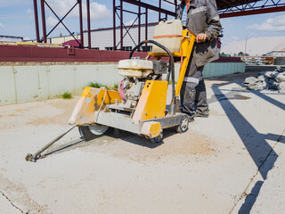 A worker at a construction site cuts concrete with a diamond saw. Concrete breaker. The device of expansion joints.