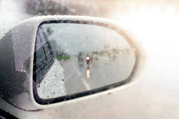 Abstract and blurred view of traffic from behind through the mirrors wing of a white car. with abstract of rainy. Wet conditions and roads.