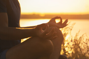 Man meditating near river at sunset, closeup