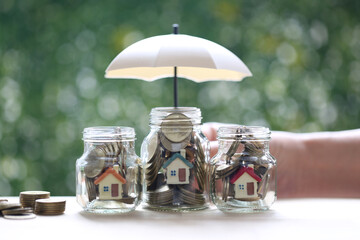 Protection,Model house and gold coin money in the glass bottle with hand holding the umbrella on natural green background, Finance insurance and Safe investment concept